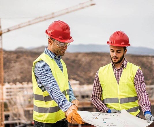 Two men in safety vests and hard hats looking at a map.